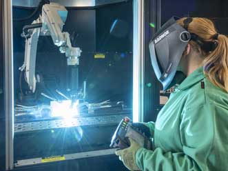 A welder in wearing a RADNOR welding helmets made by 3M Speedglas, controls an automated welding process