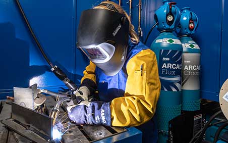 Welder welding with Arcal, EXELTOP, ARCAL Cylinders in the background.