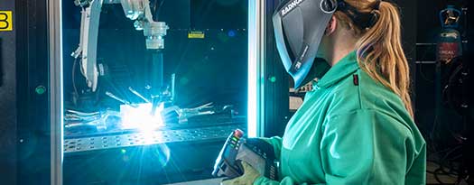 A welder in wearing a RADNOR welding helmets made by 3M Speedglas, controls an automated welding process