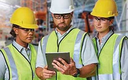 Two women and a man, stand together looking at a tablet. All wear personal protective equipment (PPE)