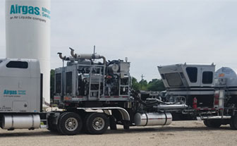 A dual-pump truck and trailer, parked infront of Airgas bulk gas containers