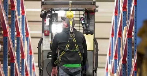 A warehouse worker wearing PPE driving a lift to retrieve products